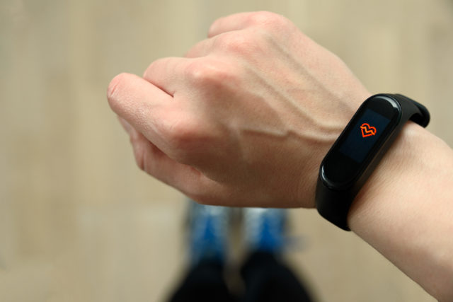 Hand with fitness tracker and sport shoes on background. Pulse mode, heart rate