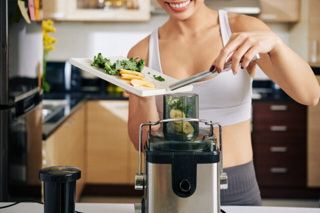 Close-up image of woman putting kale leaves, bananaand apple pieces in juicer