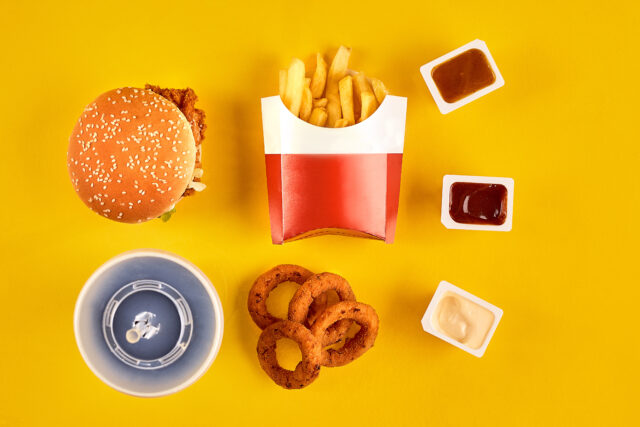 Fast food dish top view. Meat burger, potato chips and wedges. Take away composition. French fries, hamburger, mayonnaise and ketchup sauces on yellow background. Menu or receipt background. Top view. Copy space. Still life. Flat lay.