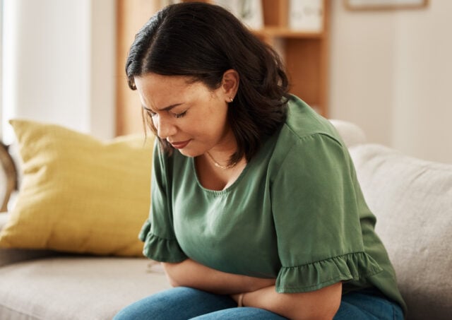 Stomach pain, stress and woman on a sofa with pms, gas or bloating, constipation or menstrual nausea at home. Gut health, anxiety and female in living room with tummy ache, anxiety or endometriosis.